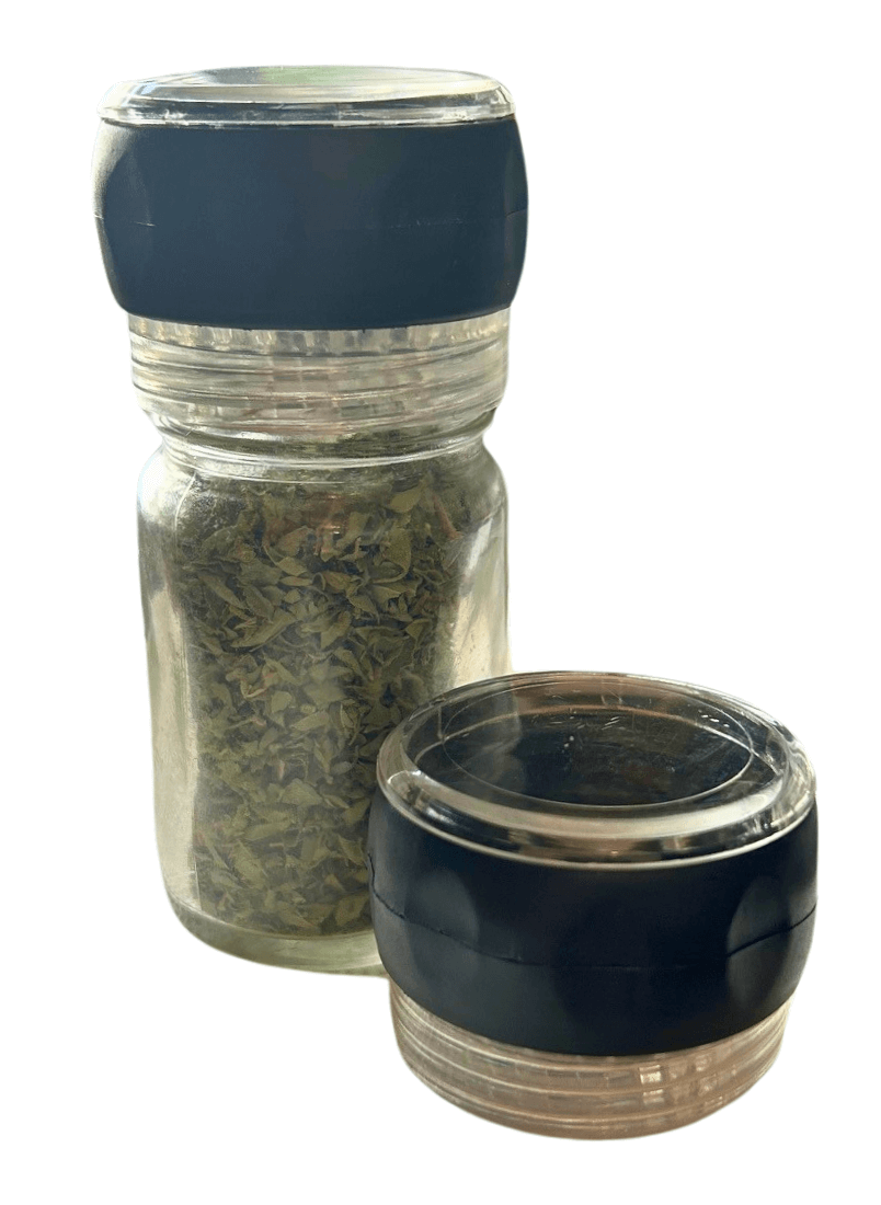 Glass jar filled with herbs with a grinder cap on top an another cap beside it