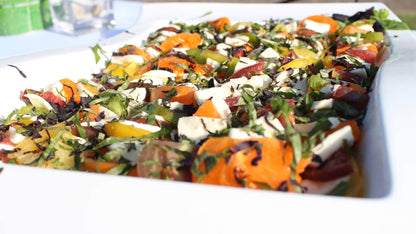 A close up of a beautiful heirloom tomato and fresh mozzarella salad with olive oil and fresh basil.