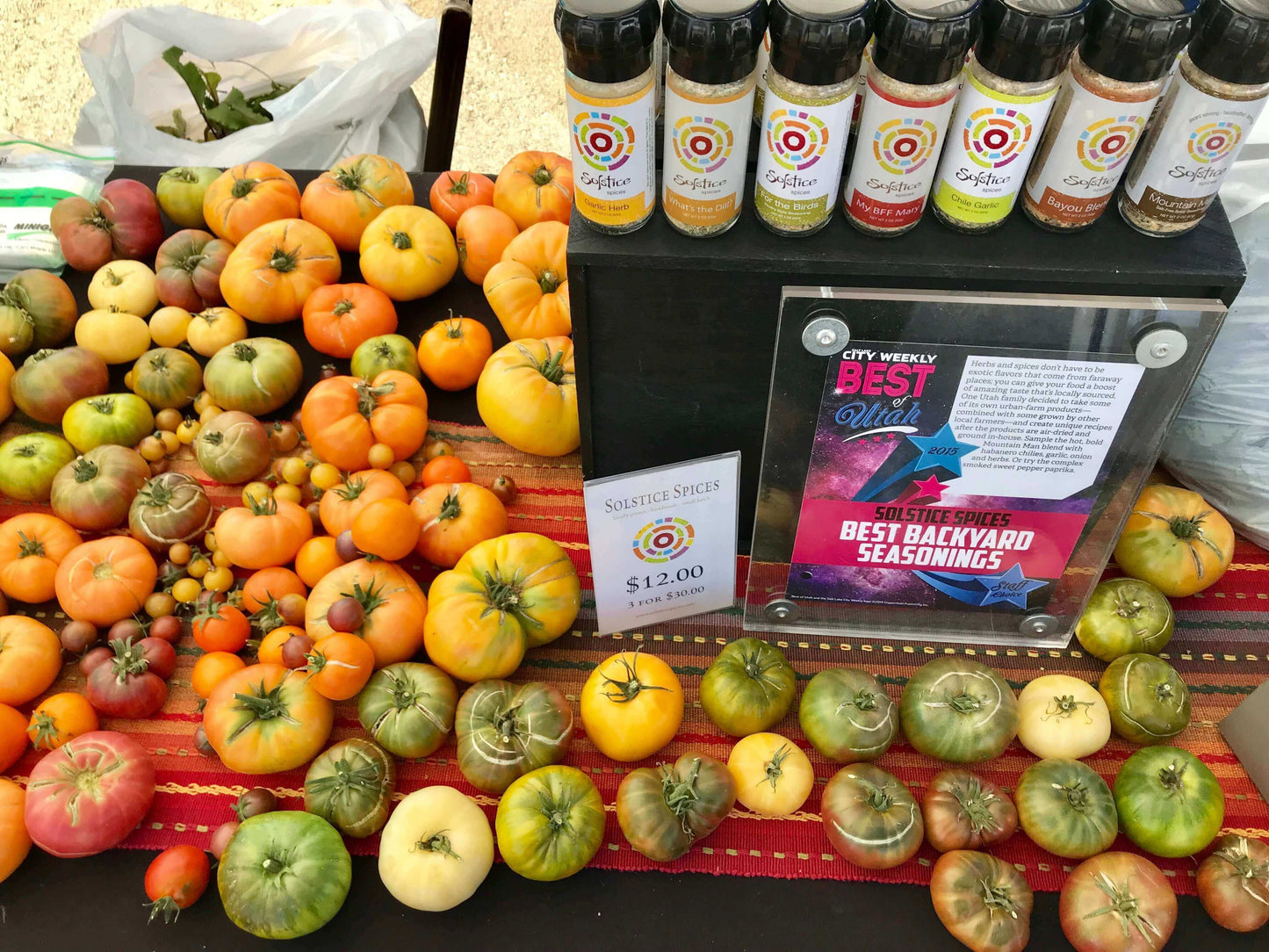 Colorful heirloom tomatoes on a table with a Best of Utah 2015 plaque and several jars of Solstice Spices on top of a black wooden box.