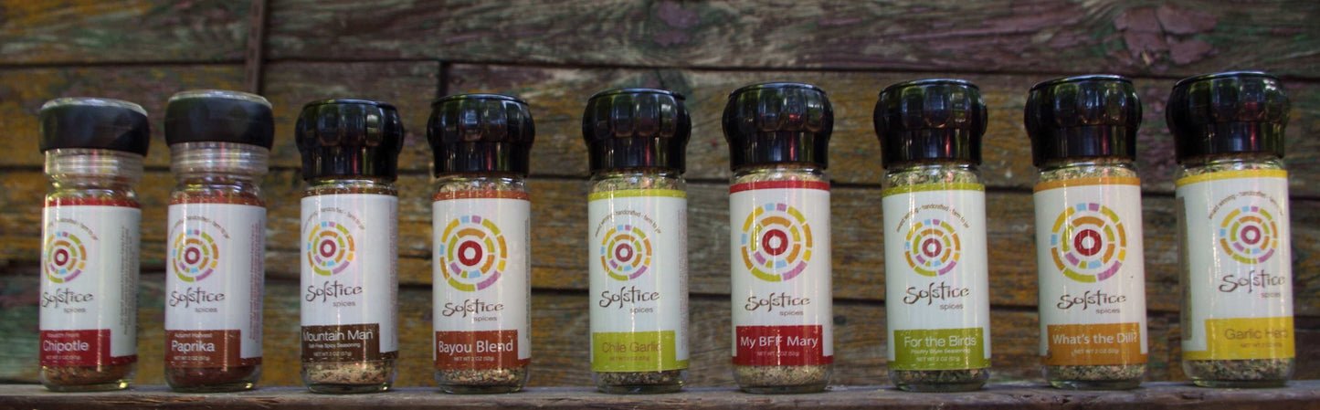 9 glass grinder jars in a row with slats of a wooden barn in the background.