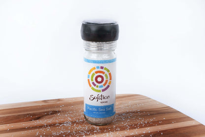 Solstice Spices Pacific Sea Salt Grinder on a wooden cutting board sprinkled with salt grains.